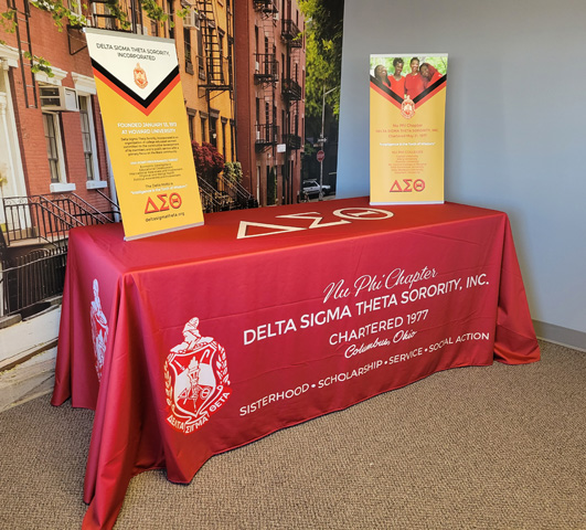 Photo depicting a red branded tablecloth for Delta Sigma Theta Sorority and two L-Tension banner stands with banners on top.  